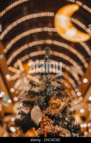 Weihnachtsbaum geschmückt mit goldenem festlichem Spielzeug und Ornamenten. Zauberhafte Neujahrsdetails, goldene Bokeh-Lichter und Mond, festlicher Winterurlaub im Feen-BAC Stockfoto