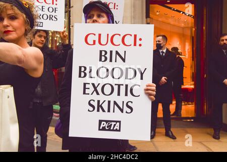 London, Großbritannien 23rd. Dezember 2021. PETA-Aktivisten versammelten sich vor dem Gucci-Laden in der Bond Street und inszenierten einen „Catwalk“ mit Handtaschen, die mit gefälschtem Blut bespritzt waren, um gegen die Verwendung von Eidechsenfellen in Guccis Produkten zu protestieren. Die Untersuchungen von PETA haben gezeigt, dass die Lieferanten von Echsenhaut deutlich unter den Tierschutzstandards liegen und für die Tiere enormes Leid verursachen. Stockfoto