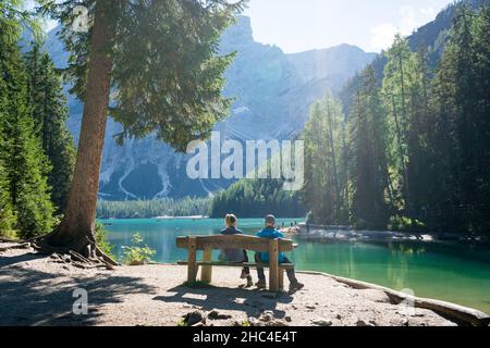 Pärchen sitzt an einem sonnigen Tag auf einer Bank am pragser wildsee im Wald der dolomiten Stockfoto