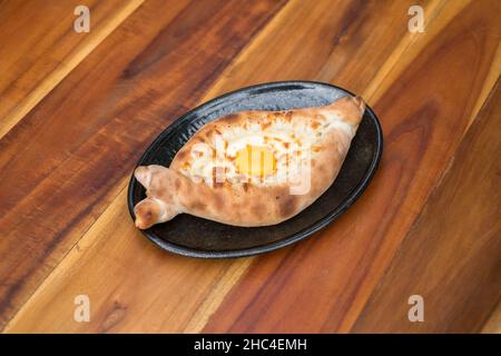 Traditionelle georgische Küche. Ajara khachapuri mit Ei auf schwarzem Teller auf Holzhintergrund Draufsicht, Nahaufnahme mit Kopierraum. Hochwertige Fotos Stockfoto