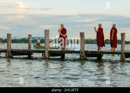 Buddhistische Mönche, die während des Sonnenuntergangs auf der U-Bein-Brücke im Taungthaman-See in der Nähe von Amarapura, in der Nähe der Stadt Mandalay in Myanmar, Burma, Südostasien, spazieren gehen Stockfoto