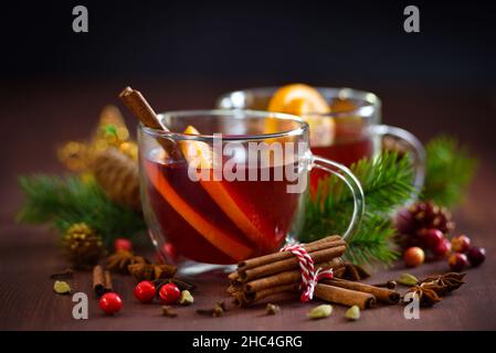 Weihnachtlicher Glühwein mit Gewürzen und Früchten auf einem rustikalen Holztisch. Traditionelles Getränk im Winterurlaub Stockfoto