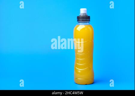 Isotonische Energie orange gelbes Sportgetränk in Plastikflasche auf blauem Hintergrund. Ermöglicht die Aufrechterhaltung des optimalen Gleichgewichts von Wasser, Salz und Elektrolyten beim Sport Stockfoto