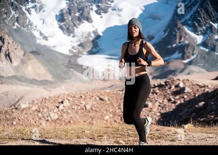Mädchen läuft auf dem Trail in den verschneiten Bergen. Stockfoto