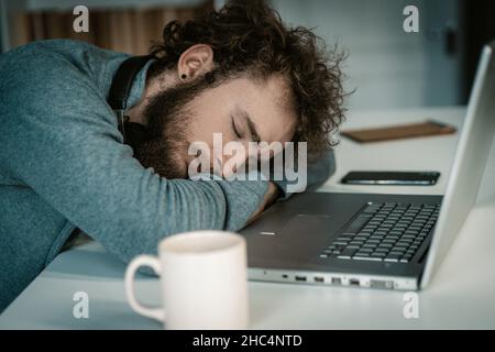 Mann mit gefalteten Händen schläft auf dem Schreibtisch mit Laptop. Schlaf im Sitzen, Freiberufler bei Nacht, Kaffeebecher auf dem Tisch. Nahaufnahme. Hochwertige Fotos Stockfoto