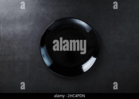 Schwarze Platte auf schwarzem Hintergrund, Draufsicht. Minimalistisches Konzept Stockfoto