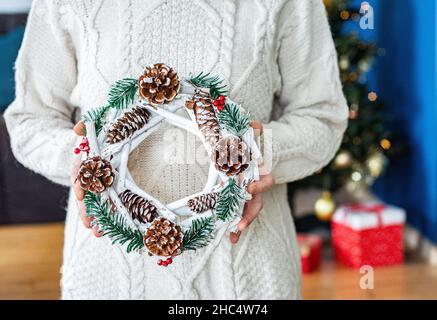 Schöner festlicher Kranz aus frischer Fichte mit Kugelspielzeug in Frauenhand. Weihnachtsstimmung. Stockfoto