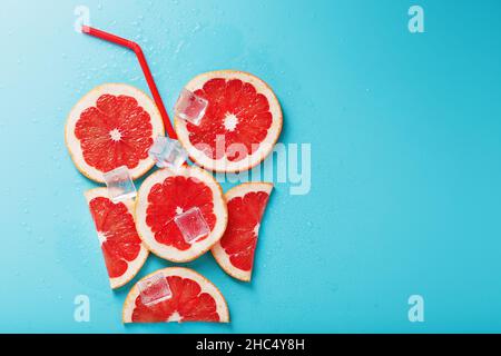 Grapefruitscheiben und Eiswürfel mit einem Strohhalm auf blauem Hintergrund in Form eines Cocktails. Das Konzept des Limonadengetränks ist eine sommerliche Erfrischung Stockfoto