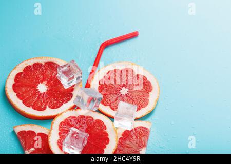 Grapefruitscheiben und Eiswürfel mit einem Strohhalm auf blauem Hintergrund in Form eines Cocktails. Das Konzept des Limonadengetränks ist eine sommerliche Erfrischung Stockfoto
