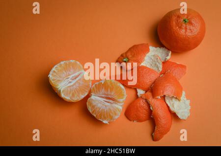 Geschälte organische Mandarine und ganze Mandarine mit Peelings auf einem orangefarbenen Papierhintergrund mit Platz für Text Stockfoto