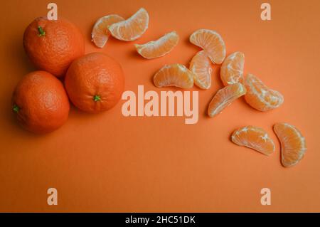 Gruppe von drei organischen Mandarinen und Fruchtkeilen auf einem orangen Papierhintergrund mit viel Platz für Kopien Stockfoto