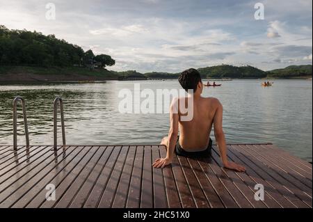 Junger asiatischer Mann, der am Abend am See relaxt Stockfoto