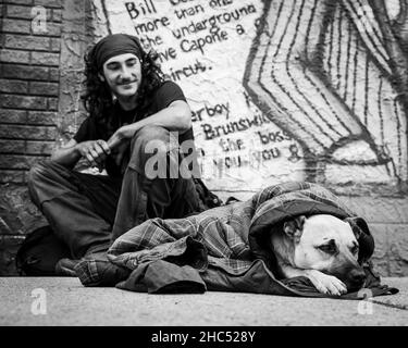 Graustufenaufnahme eines Obdachlosen und seines Hundes auf einer Straße in Moose Jaw, Kanada Stockfoto