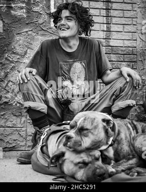 Vertikale Graustufenaufnahme eines Obdachlosen und seines Hundes auf einer Straße in Moose Jaw, Kanada Stockfoto