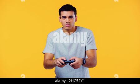 KIEW, UKRAINE - 22. DEZEMBER 2021: Junger Mann hält Joystick und spielt Videospiel isoliert auf Gelb Stockfoto