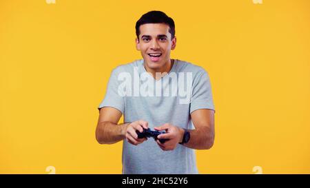 KIEW, UKRAINE - 22. DEZEMBER 2021: Aufgeregter junger Mann, der Joystick hält und Videospiel isoliert auf Gelb spielt Stockfoto