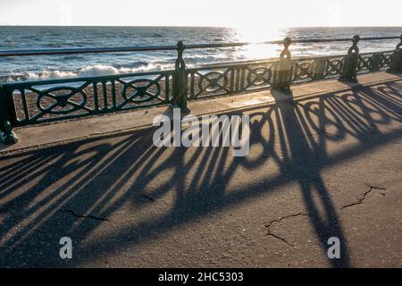 Untergehende Sonne scheint durch die Geländer entlang der Küste am Brighton Beach, Brighton, East Sussex, Großbritannien. Stockfoto