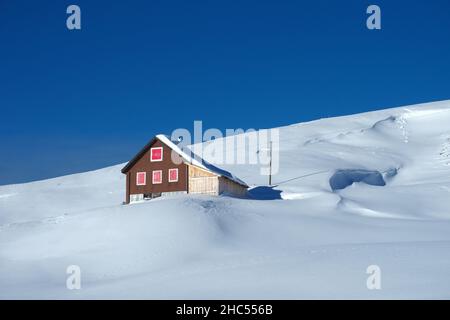 Winterlandschaft in den Schweizer Bergen: Eine wunderschöne Hütte auf schneebedeckten Bergen unter tiefblauem Himmel Stockfoto