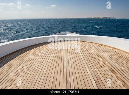 Teakholz-Bogendeck einer großen Luxus-Motoryacht auf dem Meer mit einem tropischen Blick auf den Ozean im Hintergrund Stockfoto