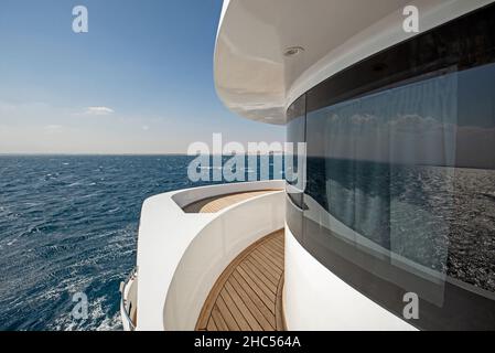 Blick vom Teakholz-Bugdeck auf eine große Luxus-Motoryacht mit tropischem Meerblick im Hintergrund Stockfoto