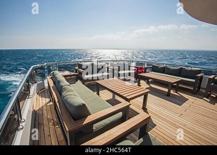 Teak Heck Holzdeck einer großen Luxus-Motoryacht Mit Sesseln, Schlafsofa und tropischem Meerblick im Hintergrund Stockfoto