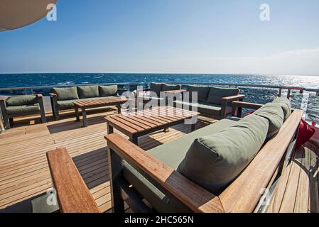 Teak Heck Holzdeck einer großen Luxus-Motoryacht Mit Sesseln, Schlafsofa und tropischem Meerblick im Hintergrund Stockfoto