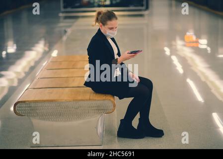 Nettes, ziemlich besorgtes junges Mädchen mit Maske und Kopfhörern in Bus, Zug oder U-Bahn, das zur Schule geht Stockfoto