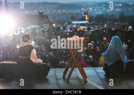 Weingarten, Deutschland. 24th Dez 2021. Kinder spielen die Weihnachtsgeschichte auf dem Vorplatz der St.-Martin-Basilika. Mehr als 200 Menschen beobachten im Regen, wie das Kind in der Krippe liegt. Quelle: Felix Kästle/dpa/Alamy Live News Stockfoto