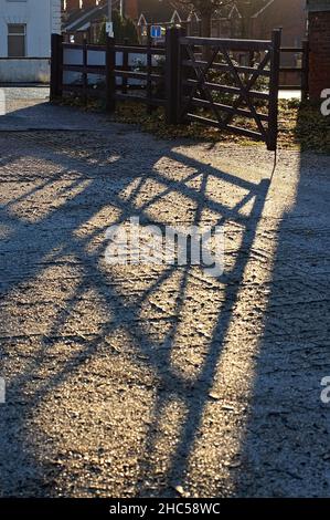 Ein offenes Holztor wirft in der frühen Morgensonne lange Schatten auf Betonboden Stockfoto