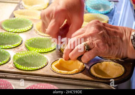 Weibliche Hände schieben Gebäck in Cupcake-Fällen in Backformen als Teil der Herstellung von Hackpasteten. Stockfoto