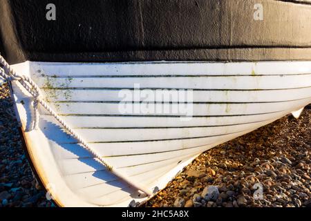 Nahaufnahme eines weißen Rumpfes mit schwarzer Verkleidung eines traditionellen hölzernen Fischerbootes, der am Strand von Worthing am Meer festgemacht wurde, 25th. November 2021 Stockfoto