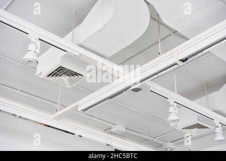 An der Decke montierte, kassettenartige Klimaanlagen mit anderen Teilen des Belüftungssystems (Rohre, Kabel und Lüftungsschlitze) in der Geschäftshalle mit Stockfoto