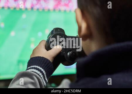 Los Angeles, USA - 21. November 2021: Ein kleiner Junge spielt Fußball auf einer Spielkonsole. Zugeschnittenes Bild eines Kindes von hinten, das Fußballspiel spielt Stockfoto