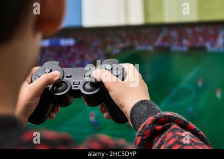 Los Angeles, USA - 21. November 2021: Ein kleiner Junge spielt Fußball auf einer Spielkonsole. Zugeschnittenes Bild eines Kindes von hinten, das Fußballspiel spielt Stockfoto