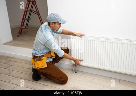 Ein Mann wechselt die Heizung im Haus, Heizkörper. Das Konzept der modernen Heizung, Ersatz der alten durch eine neue. Wärme im Haus Stockfoto