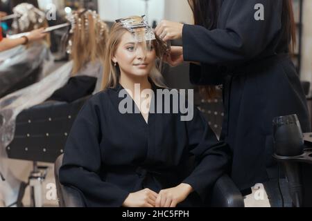 Friseur macht Bouffant mit Kamm auf dünnen Strähnen. Shatush Technik für Haaraufhellung Stockfoto