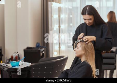 Friseur macht Bouffant mit Kamm auf dünnen Strähnen. Shatush Technik für Haaraufhellung Stockfoto