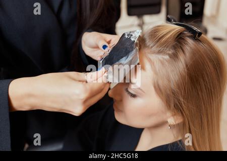 Friseur macht Bouffant mit Kamm auf dünnen Strähnen. Shatush Technik für Haaraufhellung Stockfoto