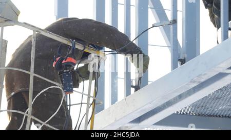 Schweißer, der mit der Elektrode beim Lichtbogenschweißen auf der Baustelle im Winter im Freien arbeitet. Schweißer-Schutzmaske arbeitet im Freien im Winter Nahaufnahme. Stockfoto