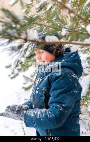 Unschärfe lächelndes Kind Junge im Winterwald im Schneesturm. Lächelndes Kind in der Nähe von Baum auf verschneiten Winterhintergrund stehen. Aktiv Zeit im Freien verbringen. C Stockfoto