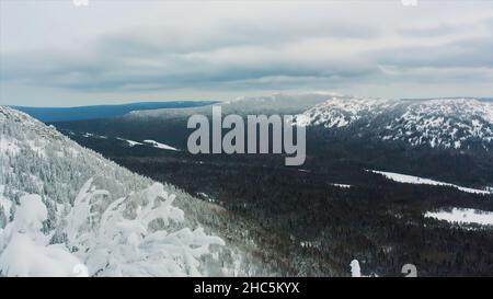 Blick auf den schneebedeckten Gipfel über dem Tal. Baumzweige im Vordergrund einer wolkigen alpinen Skyline. Video. Luftaufnahme, schöne Bäume unter t Stockfoto