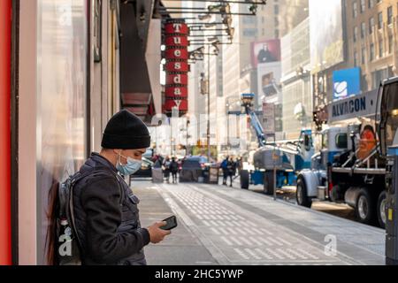 New York, Usa. 22nd Dez 2021. Ein junger Mann, der eine Gesichtsmaske trägt, überprüft sein Telefon auf der Broadway Ave in New York City während der COVID-19 pandemischen Omicron-Welle. Kredit: SOPA Images Limited/Alamy Live Nachrichten Stockfoto