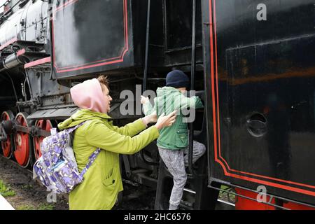 Mutter hilft ihrem Sohn, am Bahnhof auf die Lokomotive zu steigen Stockfoto