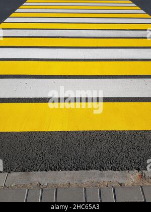 Frisch lackierter Fußgängerübergang mit gelben und weißen Markierungen auf Asphalt, vertikales Foto, Sonnenlicht. Stockfoto