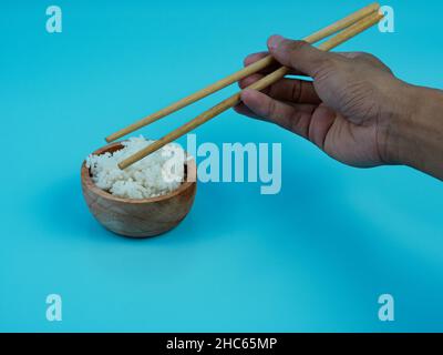 Hände, die Reis in einer kleinen Holzschüssel mit Essstäbchen nehmen. Stockfoto