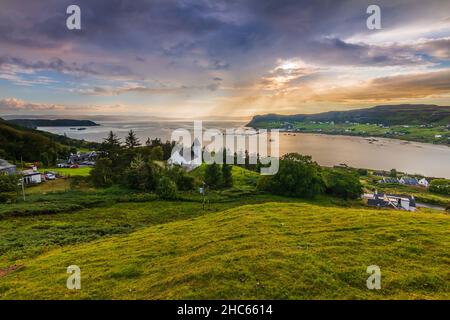 Platz in Schottland auf der Isle of Skye. Kirche auf einem Hügel mit grünen Wiesen und Bäumen. Blick über die Landschaft mit Sonnenstrahlen am Horizont. Dramatische Kl Stockfoto