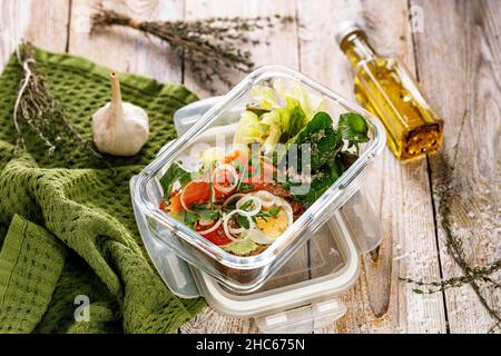 Leckeres und gesundes Mittagessen mit Lachsfischfilet in einer Glas-Lunchbox. Salat mit geräuchertem Lachs, Weichkäse, Eiern, Zwiebeln und Gemüse. Meeresfrüchte Stockfoto