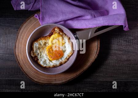 Sonnige Seite auf Eier, noch in der Pfanne, auf einem hölzernen Schneidebrett platziert Stockfoto