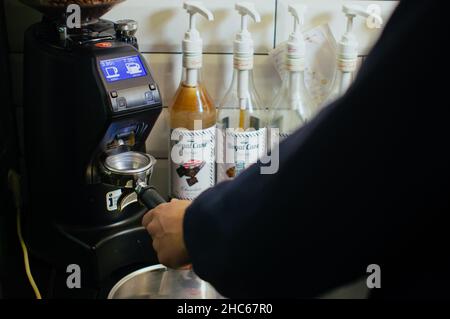 Barista bei der Arbeit. Bereitet Kaffee zu, gießt eine Kaffeebohnen, die in einer Kaffeemaschine zerkleinert wurden Stockfoto