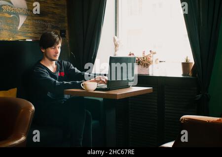 Junger freiberuflicher Kerl arbeitet an einem Laptop in einem Morgencafe Stockfoto